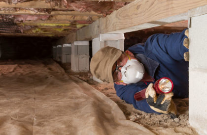 Termite inspector in residential crawl space inspects a pier for termites.